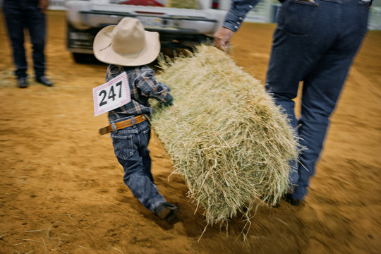 Little boy carrying a large bale of hay at a rodeo competition.