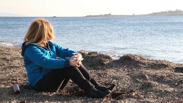 Thoughtful, pensive woman on winter sea beach sitting