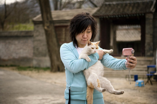Young adult woman talking a picture of herself and her cat.