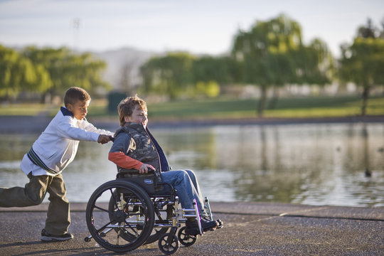 Boy pushing friend in wheelchair through park