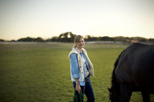 Portrait of a young adult girl standing with a horse in a field.