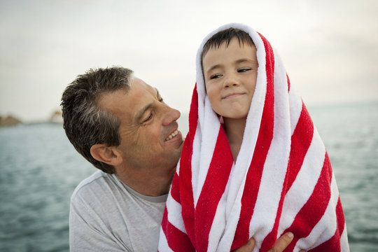 Smiling man looking at his son who is wrapped in a striped towel.