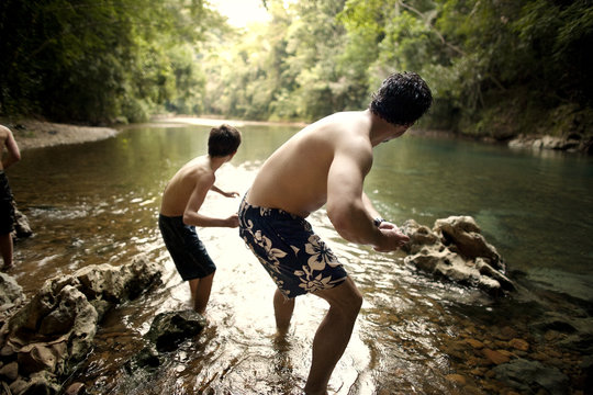 Mid adult man shows his son how to skim stones across water.