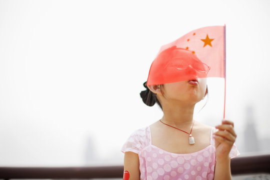 Young girl blowing a small Chinese flag.