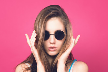 Beautiful fashionable woman in black sunglasses. Pink background. Girl in sunglasses. Round glasses. Toned image.