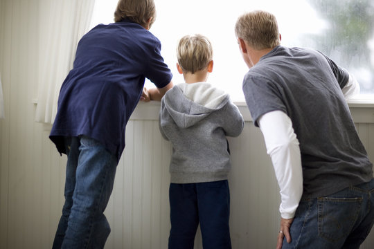 Mid-adult man looking out a window with his two sons.