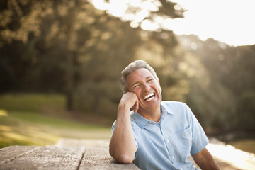 Mature man smiles as he leans on a picnic table.