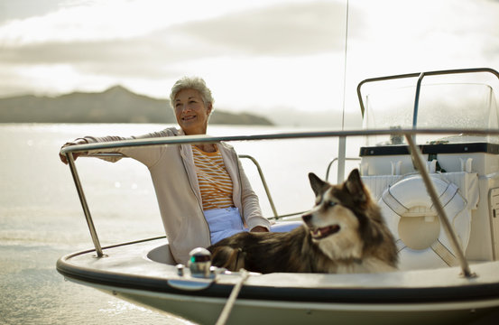Smiling mature woman relaxes on a boat with her big fluffy dog.