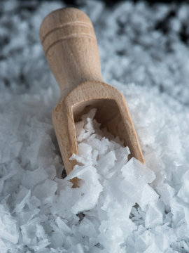 Salt flakes and wooden scoop on black background