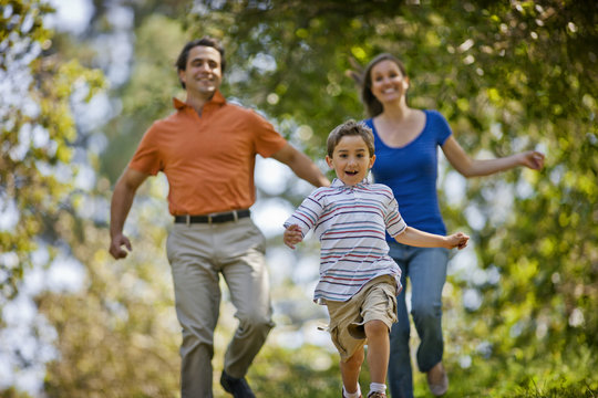 Laughing parents running after their happy young son in a park.