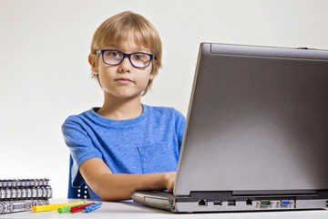 Boy with glasses using laptop computer while sitting on desk at home. Technology, education concept © vejaa