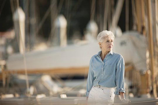 Senior woman wearing chambray shirt stands looking out at a marina.