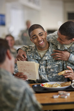 Young soldier looks over his friend's shoulder as he reads a  letter from his young son while eating breakfast in the army mess hall.