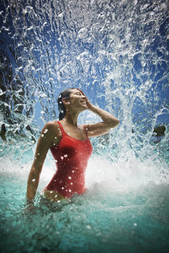 Smiling young woman standing underneath a waterfall.