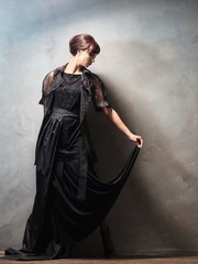 Young girl in evening dresses on grey wall.