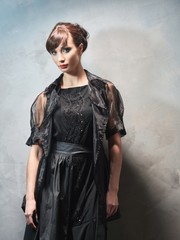 Young girl in evening dresses on grey wall.
