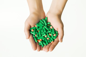 Hands is giving Green capsules and orange pills on white background.