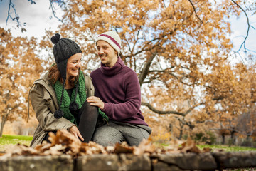 Lovely young couple talking, sit in a bench in the park in autum