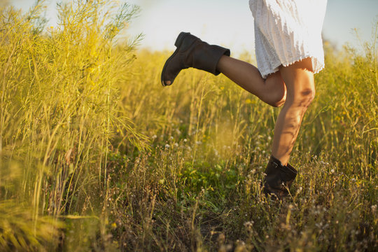 Woman in a white dress and cowboy boots dancing in a meadow.