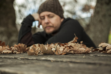 Close up leaves in a table and pensive man sitting on a bench