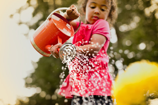Small girl watering plants with watering can in backyard.