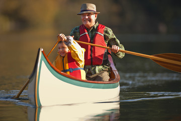 Grandfather canoeing on river with grandson.