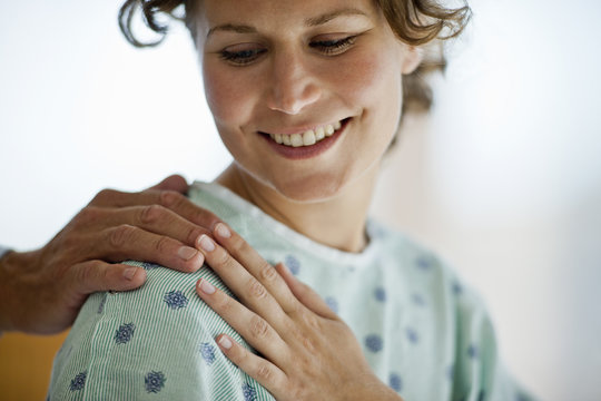Female hospital patient smiling as she touches the comforting hand laid on her shoulder.