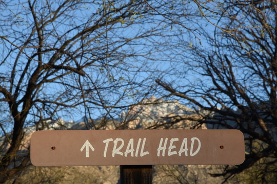 Schild an einem Wanderweg mit englischer Aufschrift "Trail Head", im Hintergrund ein schneebedeckter Gipfel
