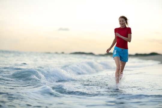 Mid-adult woman running in water at the beach.
