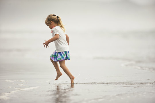 Happy young girl playing in shallow water on a beach.