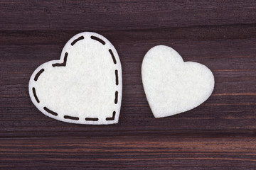 Fototapeta premium Two white hearts of felt on a brown wooden background. Valentine Day. Greeting Card.