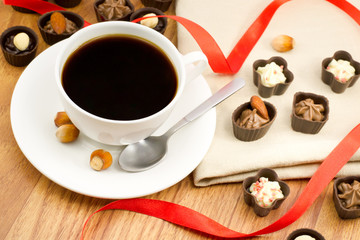 white cup of coffee with chocolates and wood nuts on burlap clos