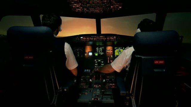Landing of passenger plane. Sunset view from the cabin of modern plane to the runway during landing. Airport lighting. Two professional male pilots in the cockpit or flight deck control passenger