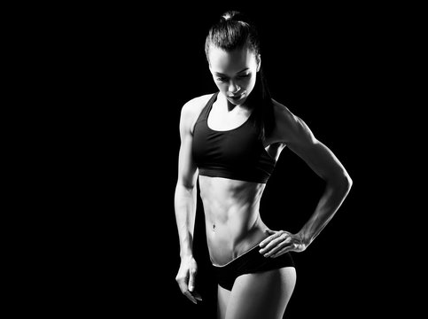 Young sporty woman posing on black background. Black and white photo