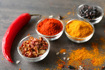 Aromatic spices in glass bowls on grey background