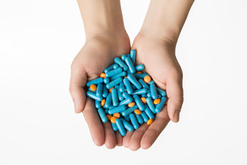 Hands is giving blue capsules and orange pills on white background.