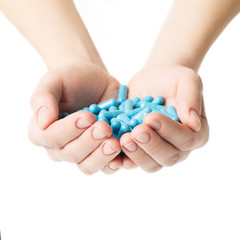 Hands is giving blue capsules and orange pills on white background.