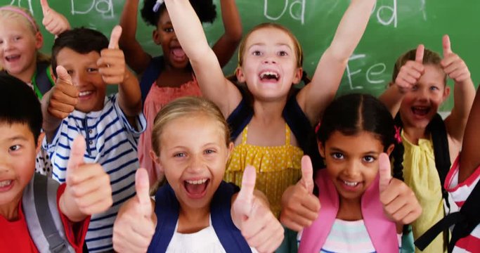 Portrait of school kids showing thumbs up in classroom at school 4k