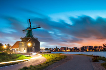 Typical Netherlands landscape, traditional Dutch Windmills and wooden agricultural buildings over water on evening