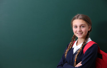 Teenage girl with backpack standing near green school blackboard