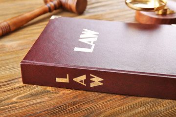 Law book with judge gavel and scales on wooden table