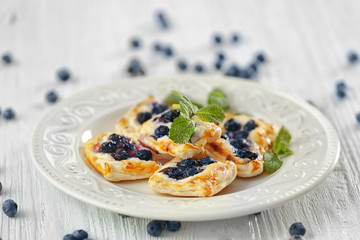 Sweet tasty pastries and fresh bilberries on plate against wooden background