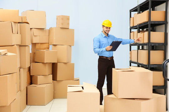 Man holding clipboard and pointing on cartoon box at warehouse