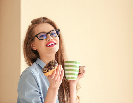 Beautiful young woman with tasty donut and cup of coffee on color background