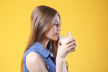 Beautiful young woman drinking milk on yellow background