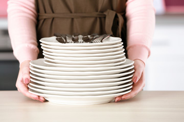 Young woman with pile of dishware on kitchen, closeup