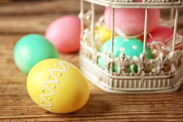 Colourful Easter eggs and decorative cage on wooden table