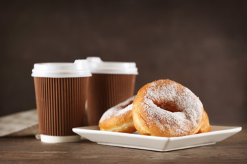 Tasty donuts with cups of coffee on table