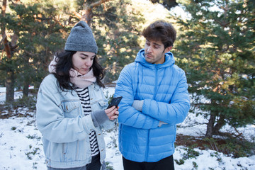 Young caucasian white woman chatting with mobile phone as she passes from her boyfriend in the...