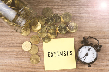 Coins spilling out of a glass jar with EXPENSES text on wooden background. Financial Concept